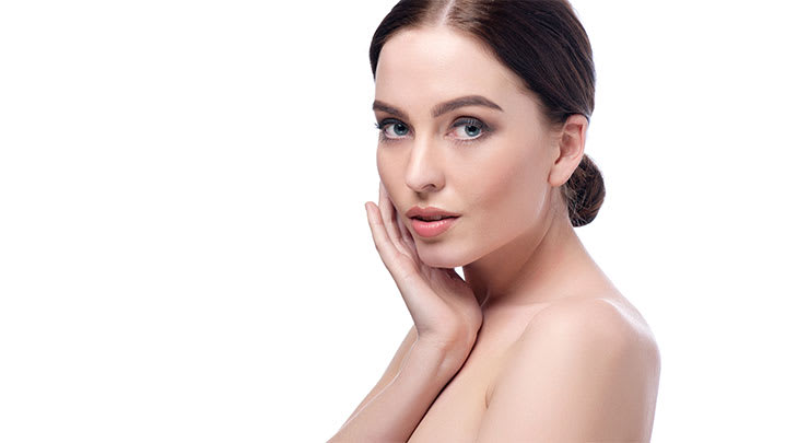 Woman with brown hair and beautiful skin touching her face.