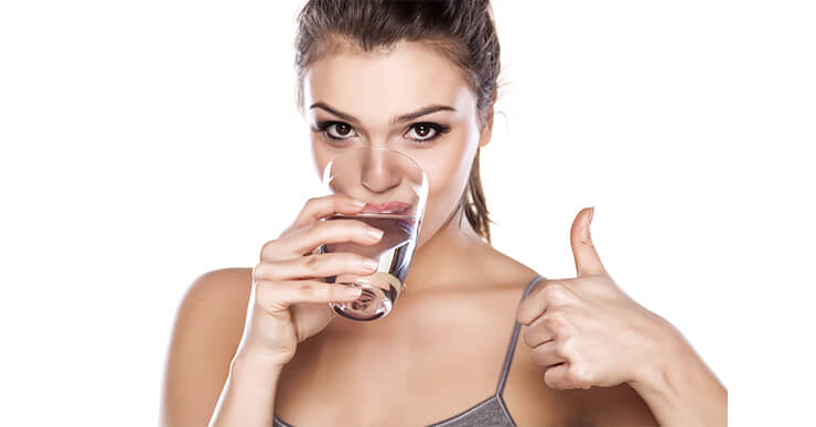 Woman giving thumbs up while she drinks water to lose weight.