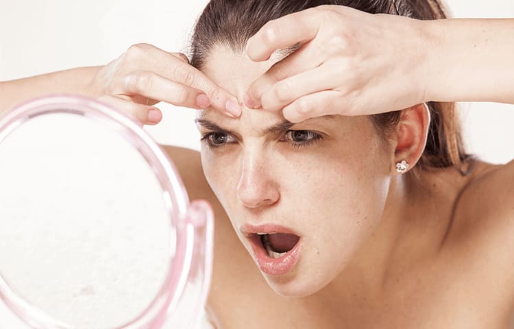 woman mad at her reflection in the mirror popping pimple