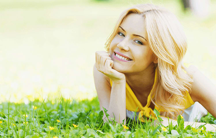 blonde woman lying on front in grass smiling with face resting in hand