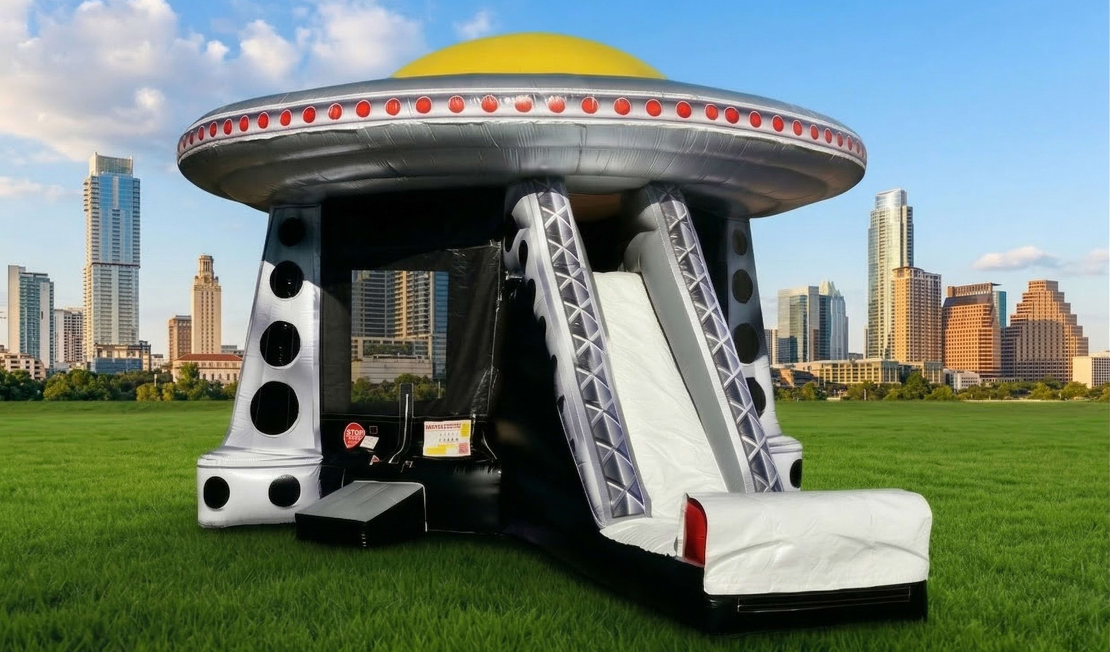 A dynamic, eye-catching image featuring a large, sci-fi-themed alien spaceship inflatable bounce house and slide setup in a sprawling urban park, with the recognizable skyline of downtown Austin, Texas, including its unique skyscrapers like the "Jenga" In