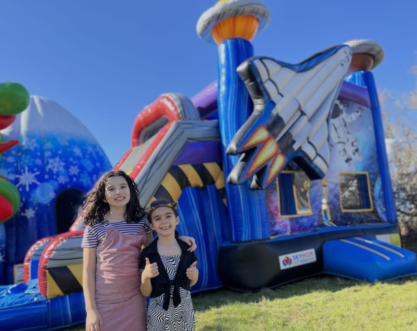 Susy and Veronica in front of a Sky High Party Rentals space combo bounce house