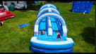 Summer fun in the sun: Kids racing down a massive 32-foot double-lane water slide at a backyard birthday party. The blue and white inflatable features water-spraying arches and dual sliding lanes, surrounded by family, balloons, and party treats under a c Youtube