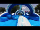 Summer fun in the sun: Kids racing down a massive 32-foot double-lane water slide at a backyard birthday party. The blue and white inflatable features water-spraying arches and dual sliding lanes, surrounded by family, balloons, and party treats under a c Youtube