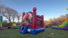 An action-packed backyard birthday party scene featuring a large Spider-Man inflatable bounce house combo with a red and blue slide. Families are gathered on the lawn, with adults chatting and children enjoying cotton candy and snow cones at nearby tables Youtube