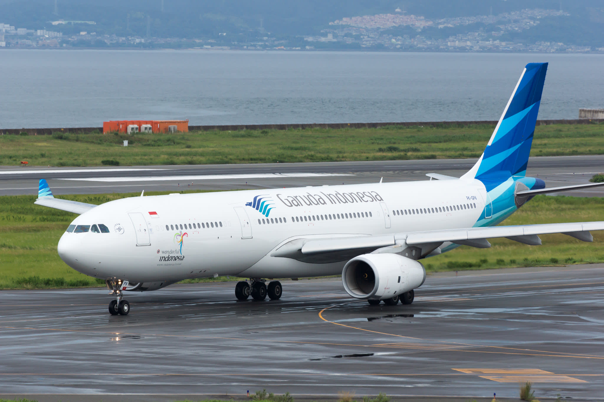 Garuda Indonesia commercial aircraft flying over city skyline