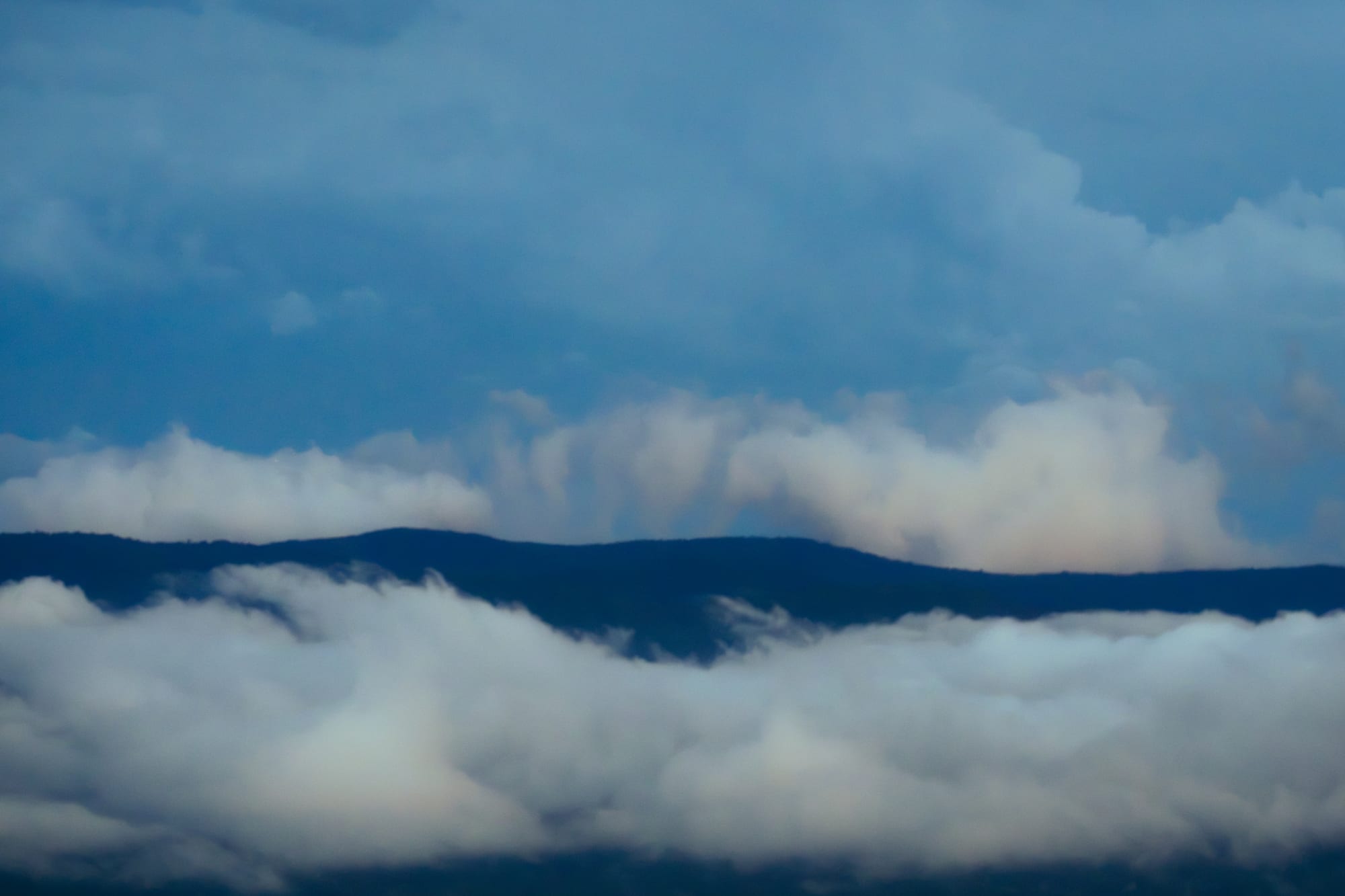 Low fog runs the width of a valley at dawn, catching first light before the sun clears the ridge.