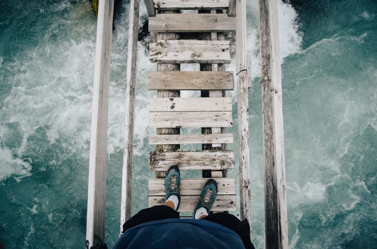 Feet standing on a bridge over water