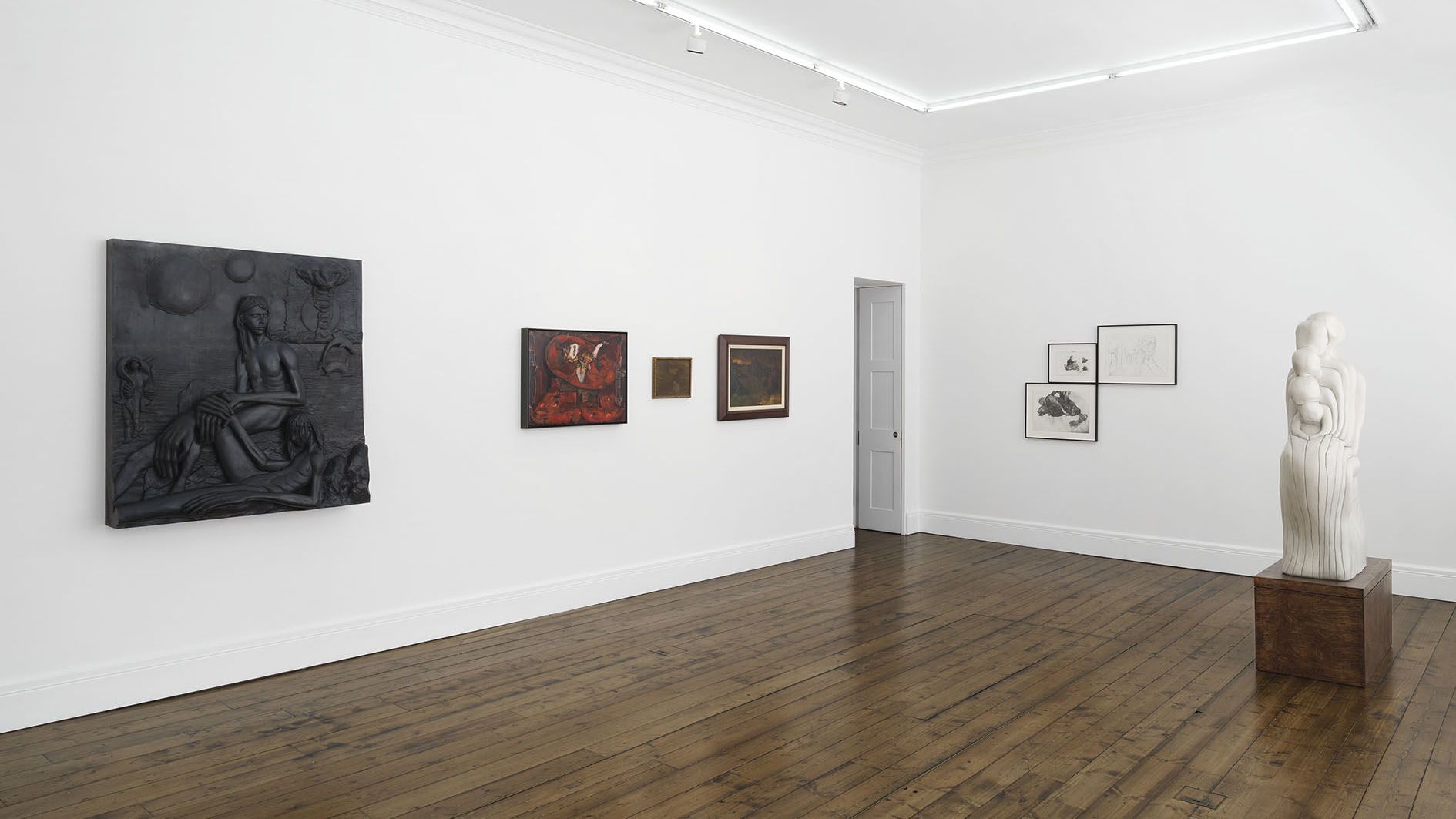 Gallery room with white walls and wooden floors displaying various artworks including paintings and a white sculpture on a pedestal.