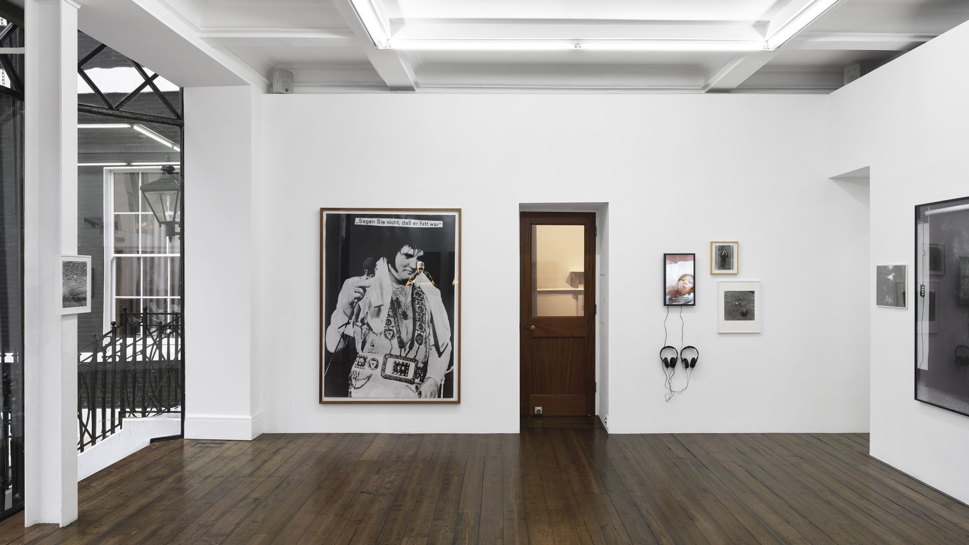 Gallery space showing large Elvis Presley portrait with German text overlay, small framed works, and doorway to adjacent room