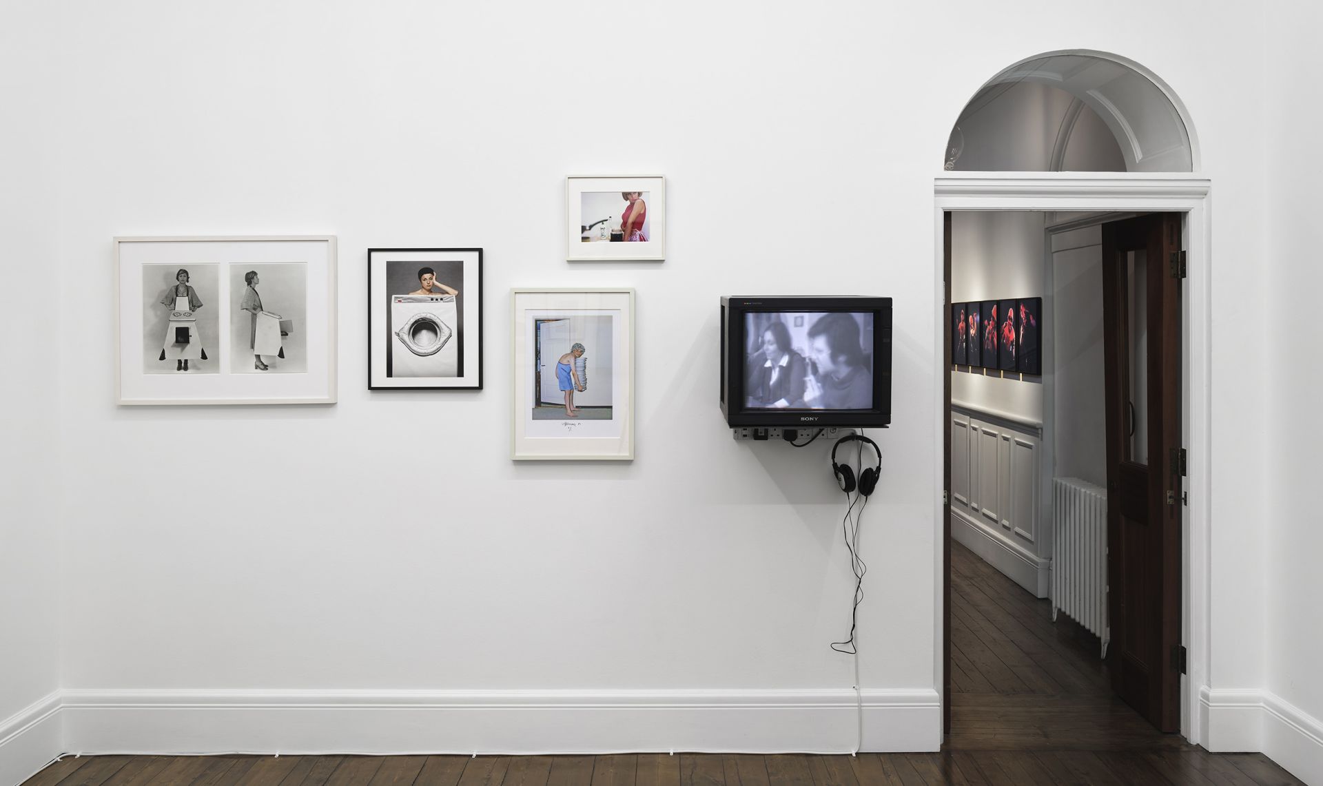 Gallery wall with photographs including fashion images, domestic scenes, and mounted TV monitor with headphones
