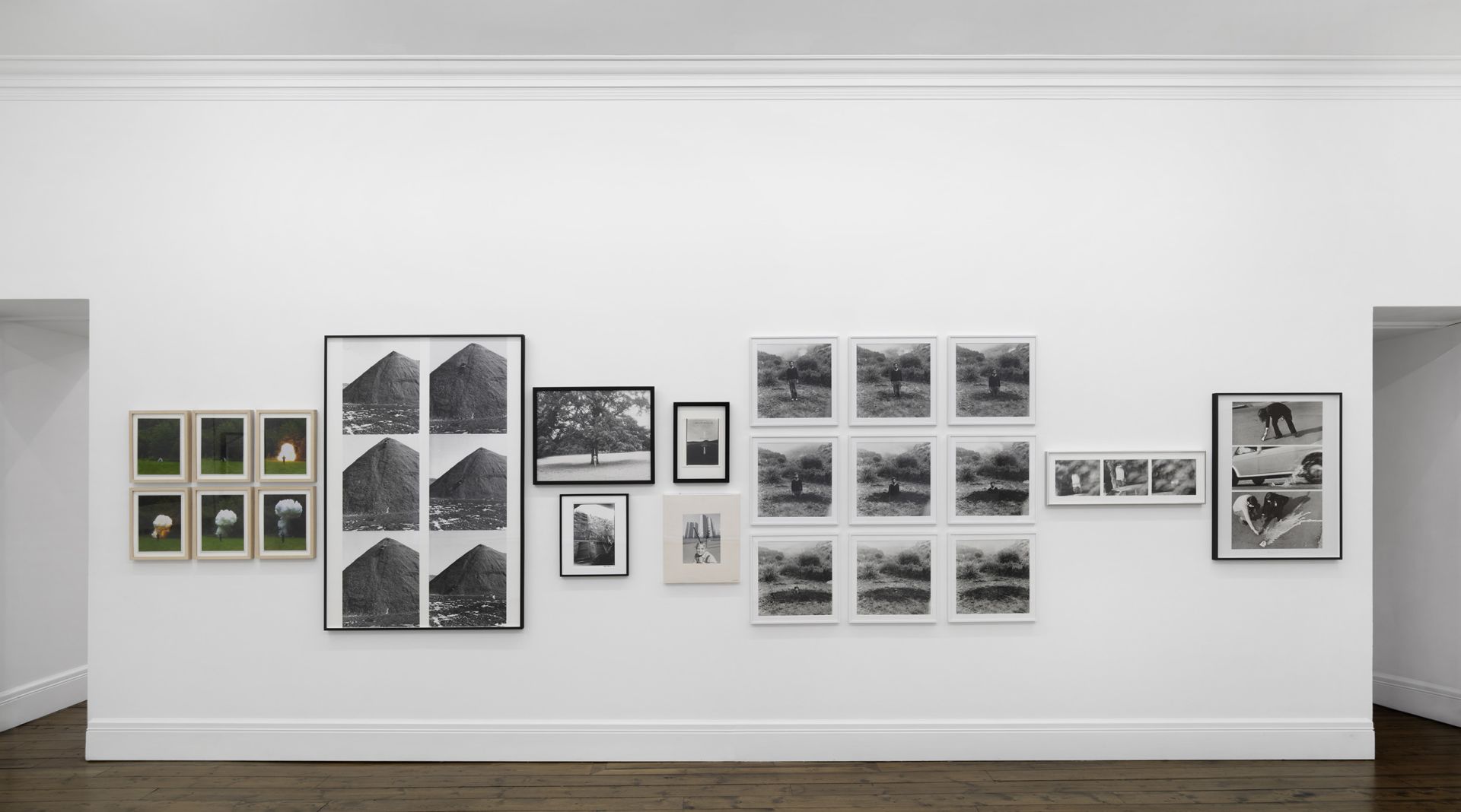 Gallery wall with various framed photographs including coal piles, trees, and figures in natural settings.