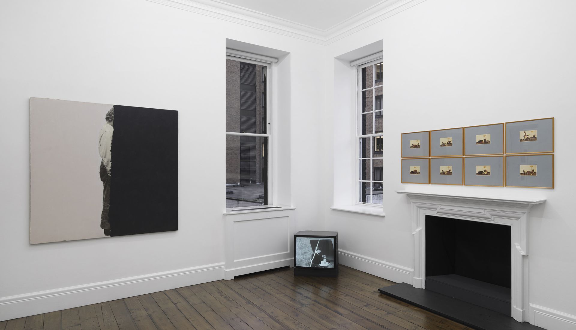 Gallery room with large painting showing black rectangle obscuring figure, plus grid of small photos and a video monitor.