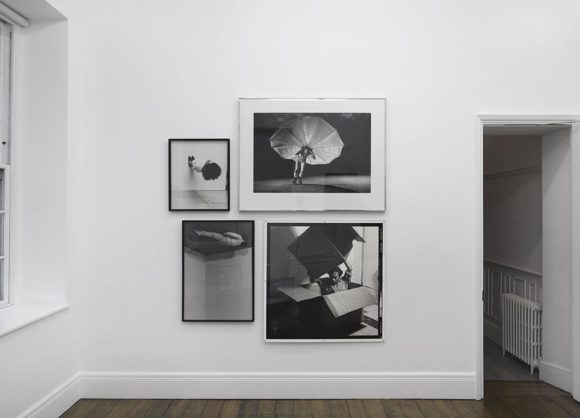 Four black and white photographs showing performance art with umbrellas, body parts, and geometric shapes.