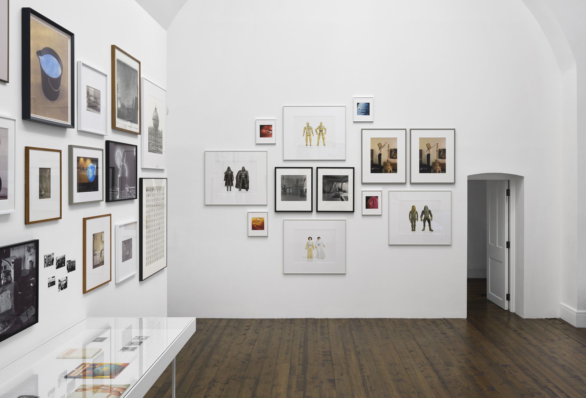 Gallery wall with diverse collection of framed photographs, illustrations, and small toy figures mounted in salon-style arrangement