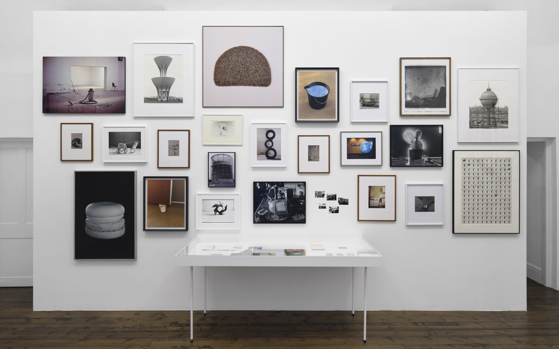 Salon-style gallery wall featuring various photographs of everyday objects, food, and architecture above a display case