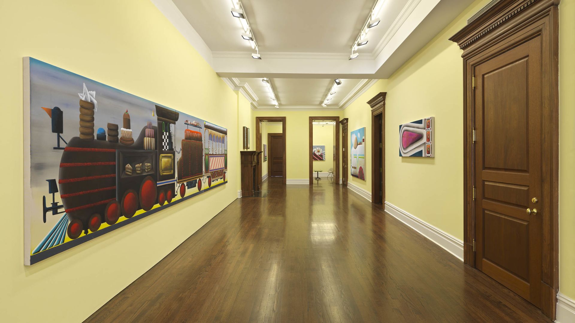 Gallery hallway with yellow walls displaying large colorful paintings, including a wide candy train triptych on the left.