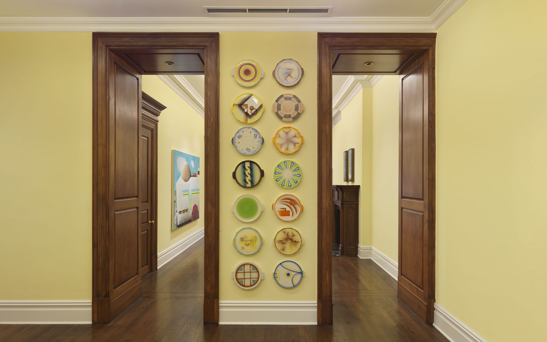 Gallery wall between two doorways displaying ten round painted cake and pie artworks arranged in two vertical columns.