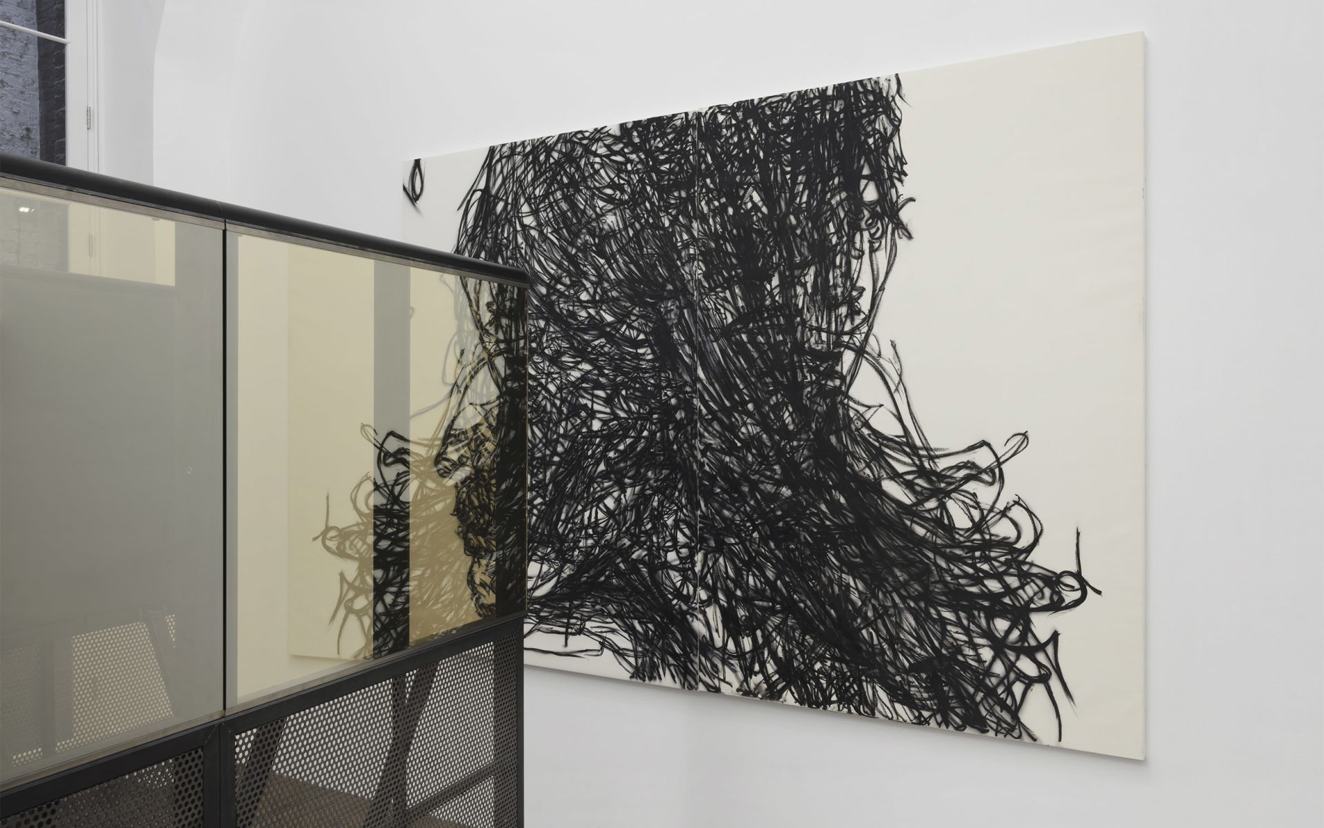 Gallery view: large diptych of dense black scribbled lines forming a head, beside a black metal installation with glass panels.