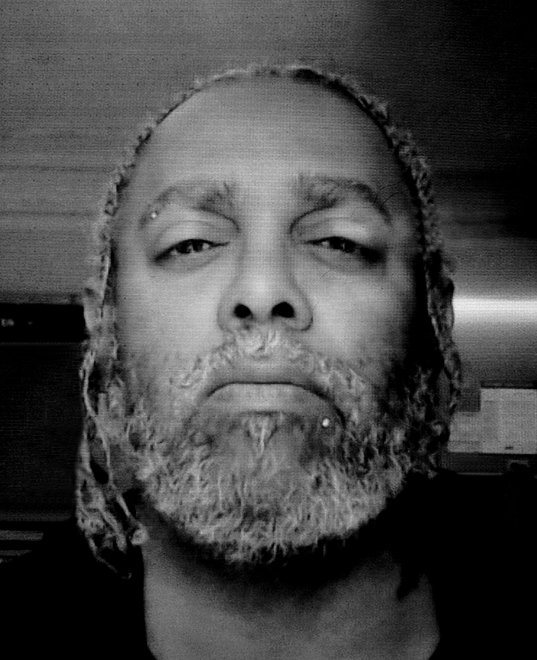 Black and white selfie portrait of a person (Arthur Jafa) with braided hair and a beard looking directly at camera