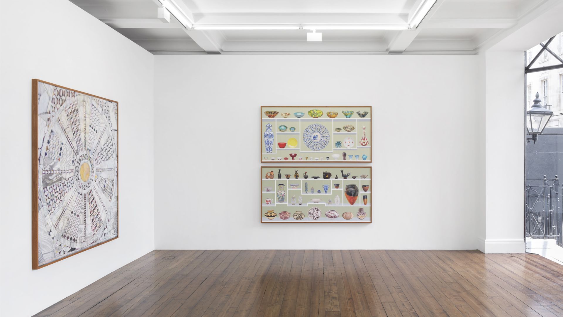 Gallery wall showing geometric mandala-like artwork and collection displays of ceramics, bowls, and decorative objects in grid arrangements