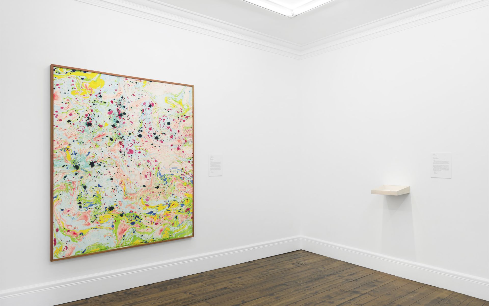 Abstract expressionist painting with vibrant splatters and drips in yellow, pink, green, and black on light background