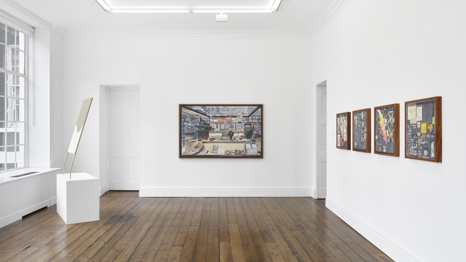 Gallery view with sculptural mirror piece, large cabinet artwork, and four smaller framed works on white walls