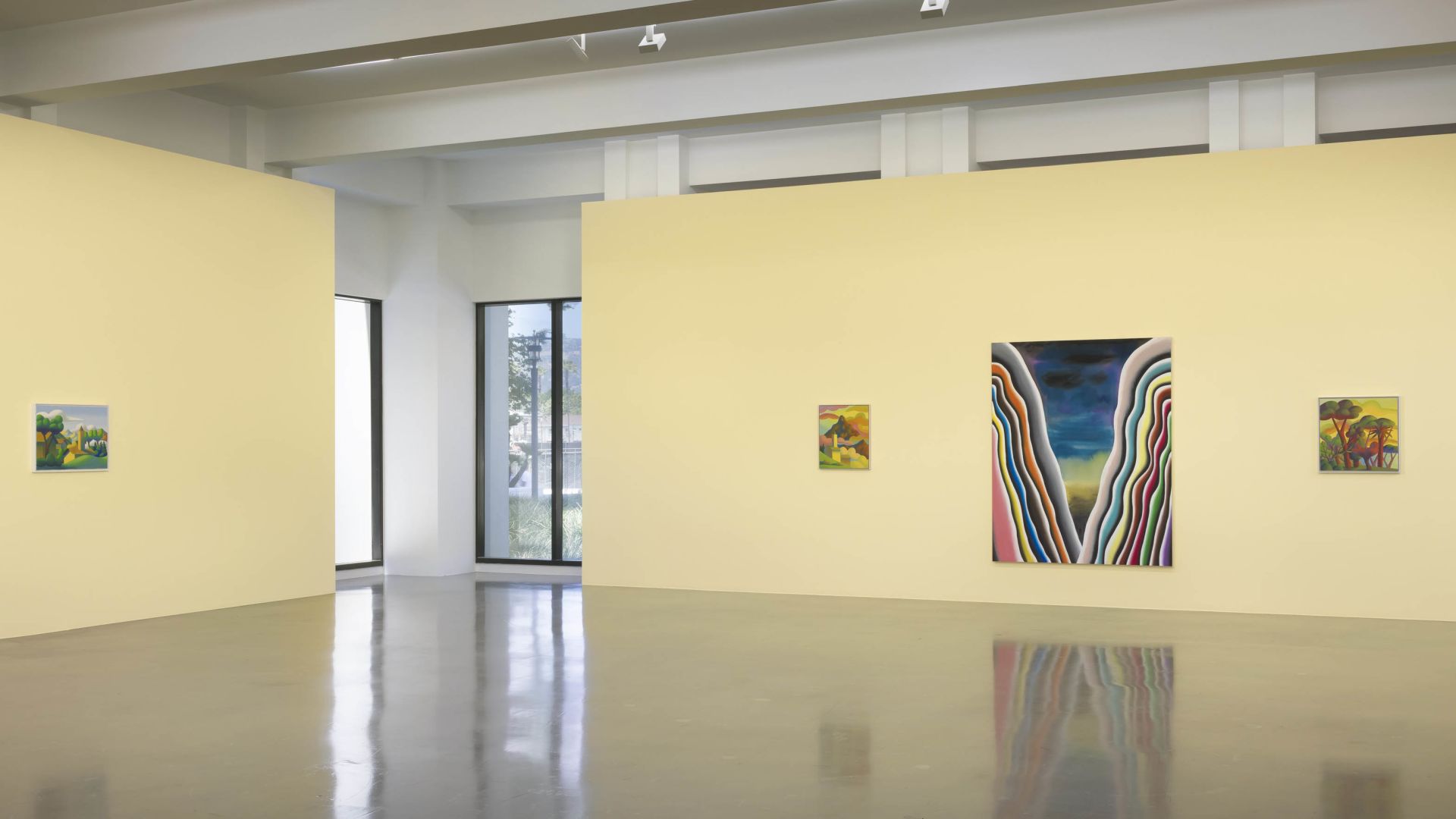 Gallery interior with cream walls displaying various small landscape paintings and one large colorful striped abstract work
