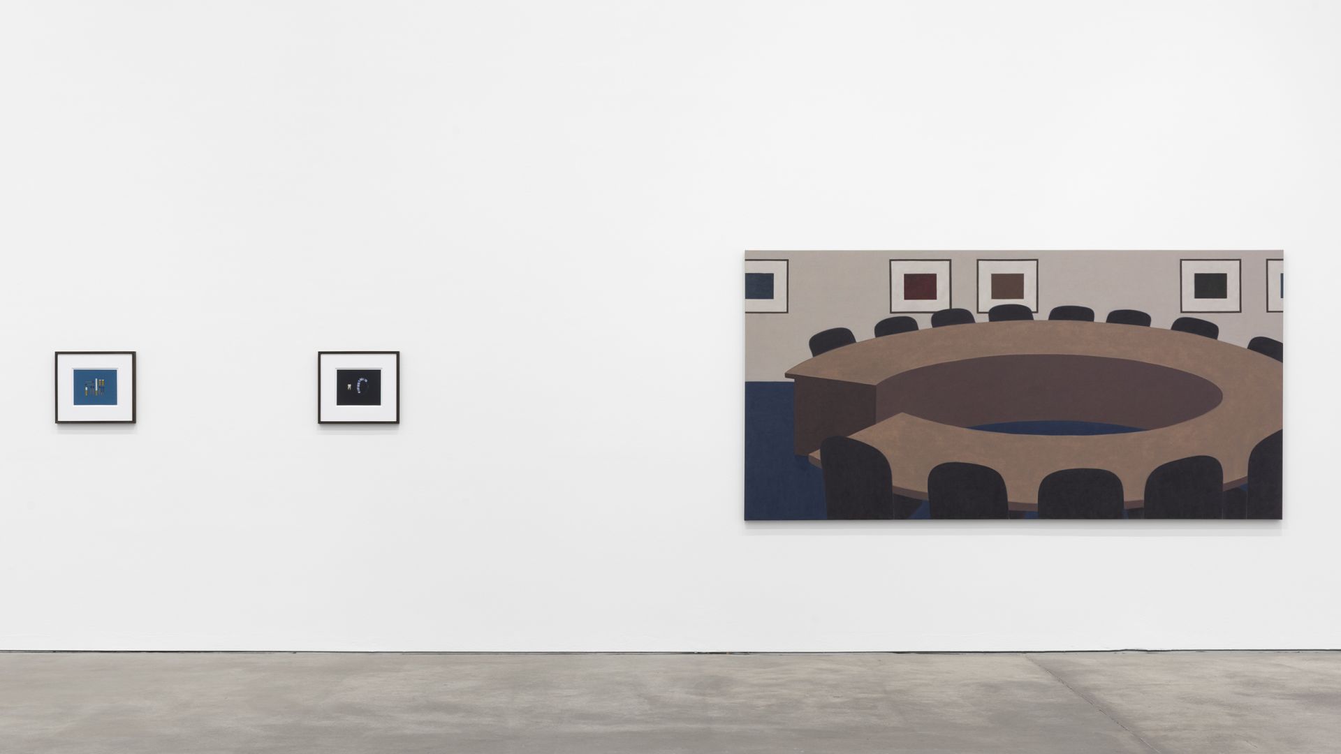 Gallery wall showing small framed works and large painting of oval conference table with chairs and wall art.