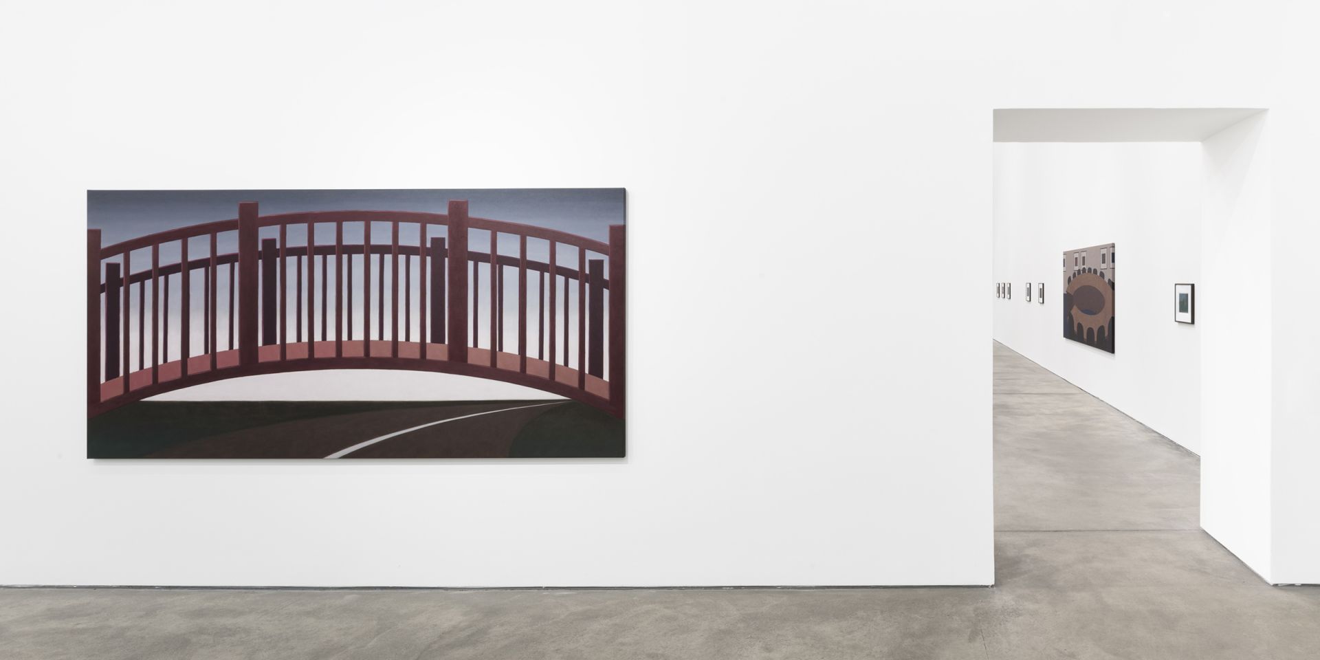 Gallery view showing white walls with paintings including a large red bridge and geometric works, with doorway leading to adjacent room.