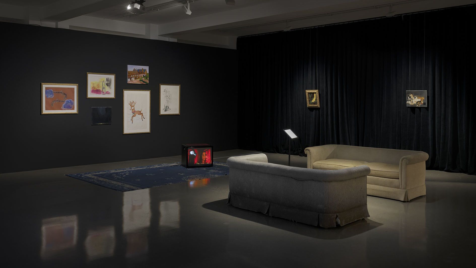 Gallery interior with dark walls displaying framed artwork and sketches, featuring seating area with sofas.