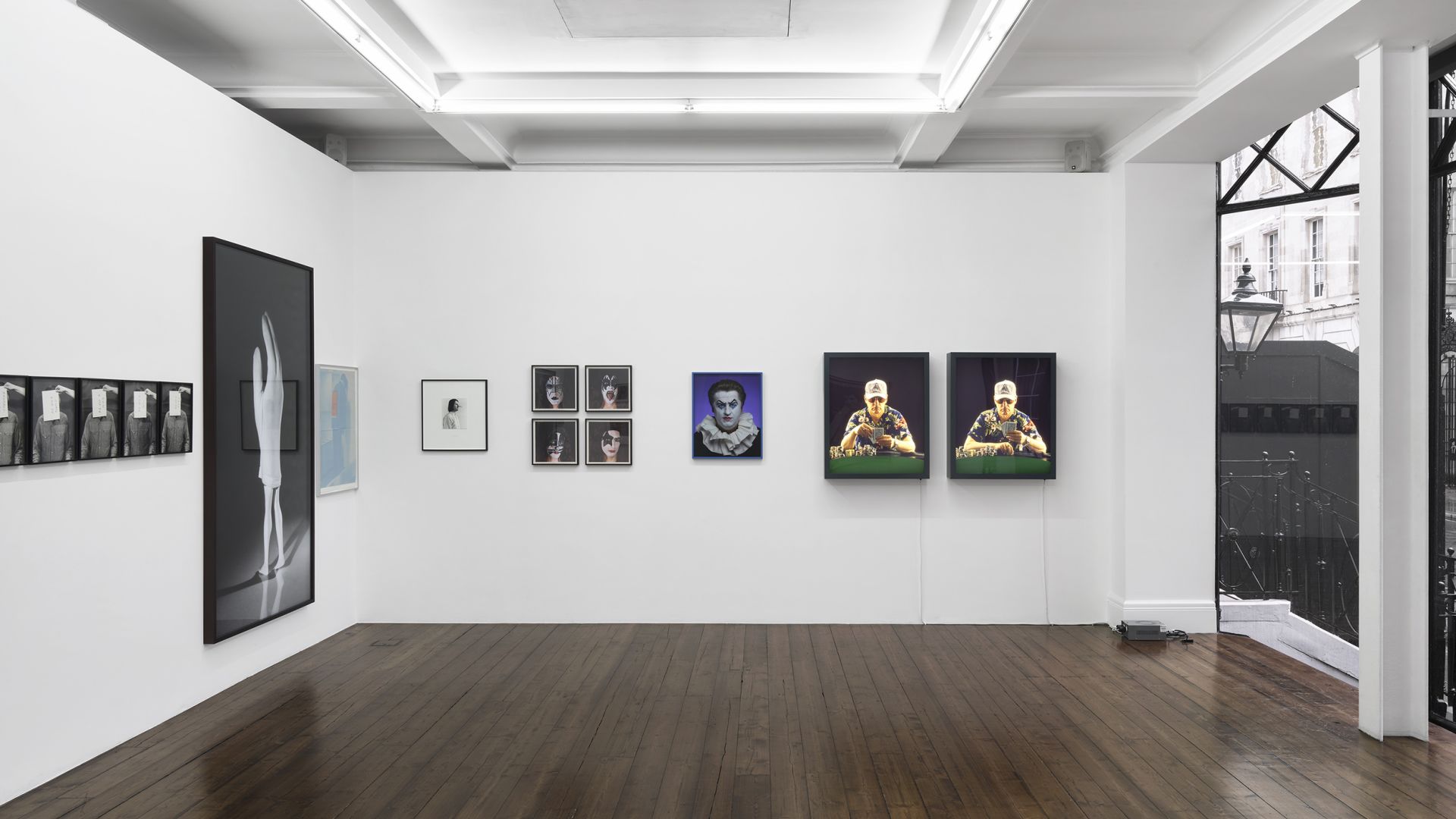 Gallery wall displaying various framed artworks including portraits, a large body image, and colorful pieces in white exhibition space