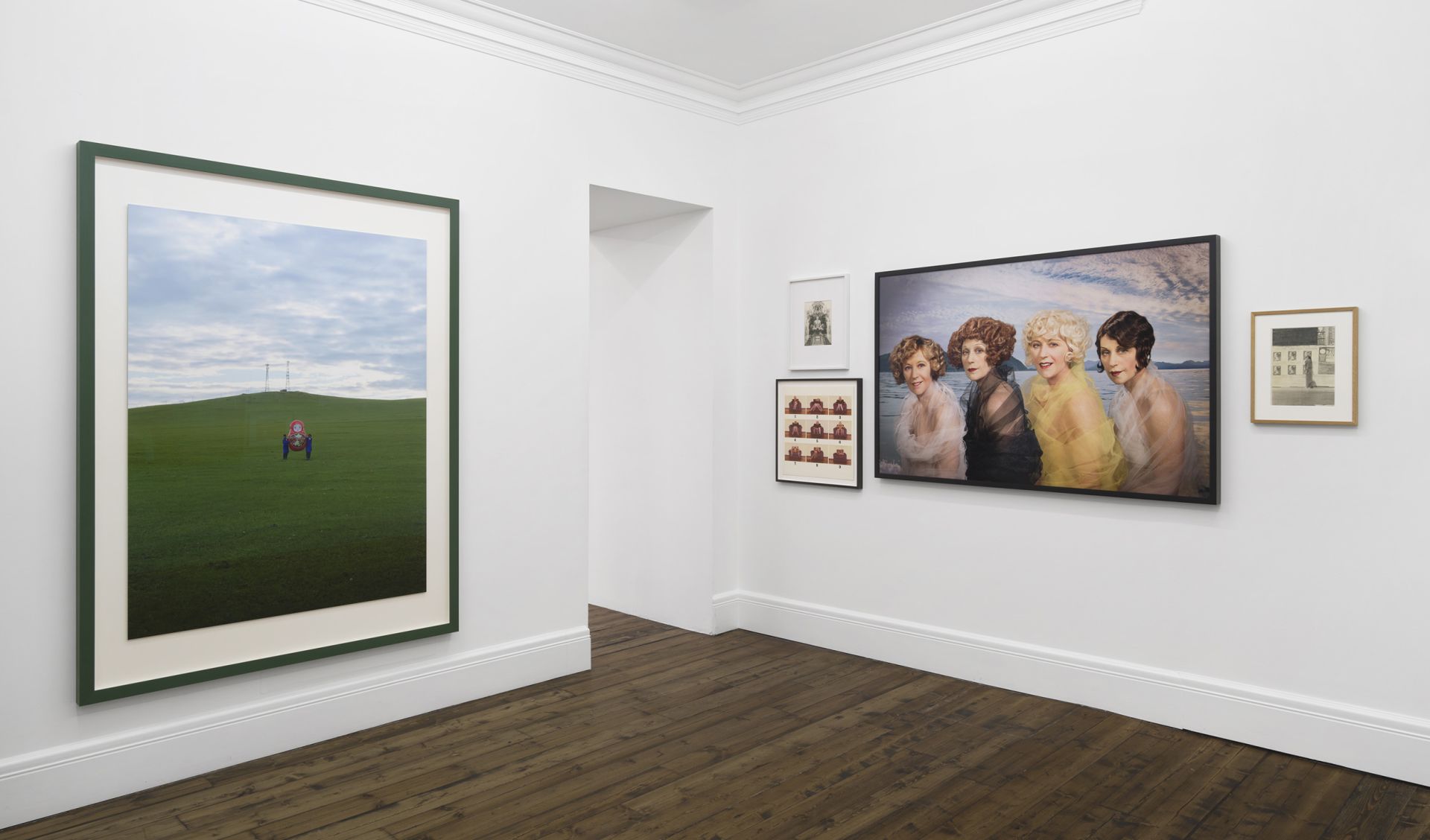 Gallery wall with landscape photograph, vintage hairstyle photograph, and smaller framed works in modern exhibition space
