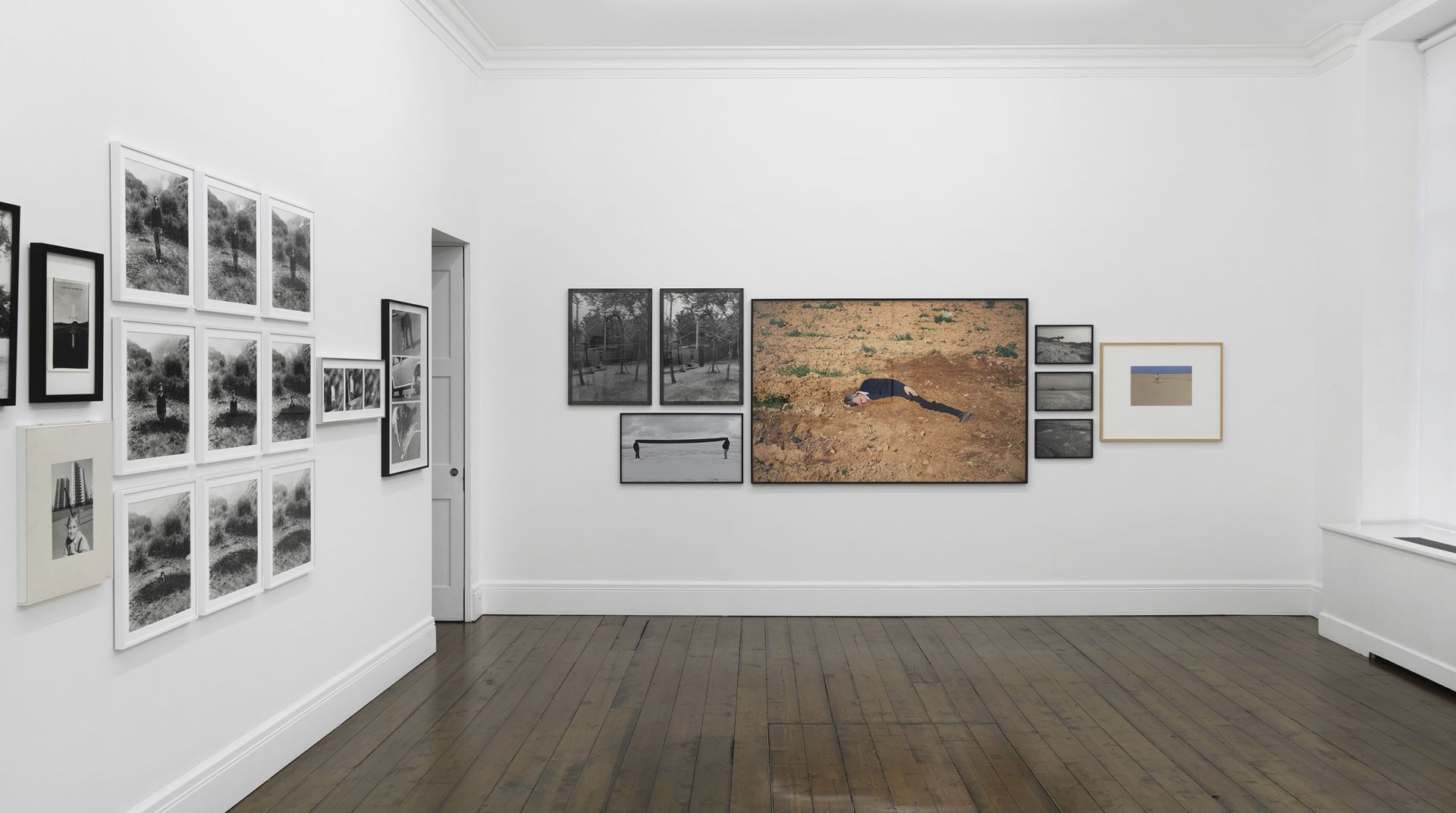 Gallery wall displaying multiple framed photographs including landscapes, a figure on red earth, and various black and white images.