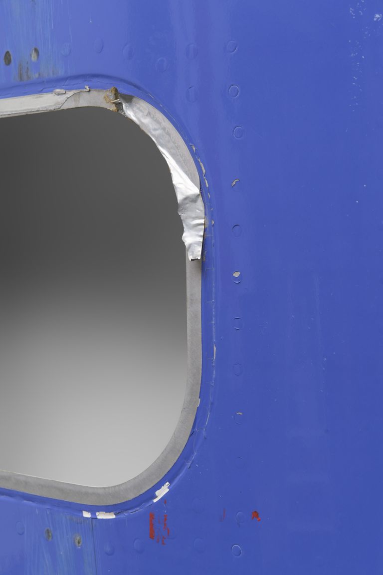 Blue panel with four rounded rectangular cutouts, appearing to be repurposed aircraft or industrial material with red and white striped detail at bottom