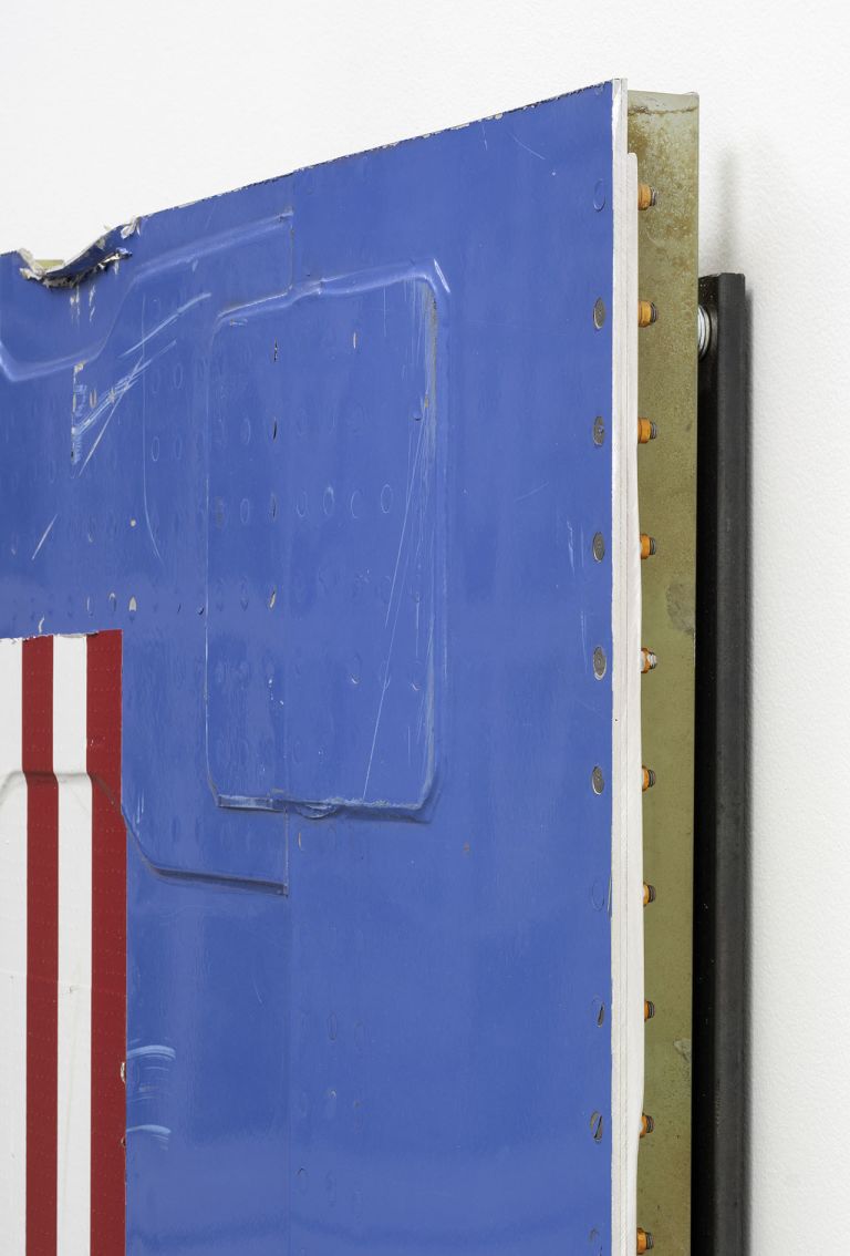 Mixed media artwork with blue background, red and white stripes, and two square-shaped cutouts. The piece appears to incorporate industrial materials with metal borders