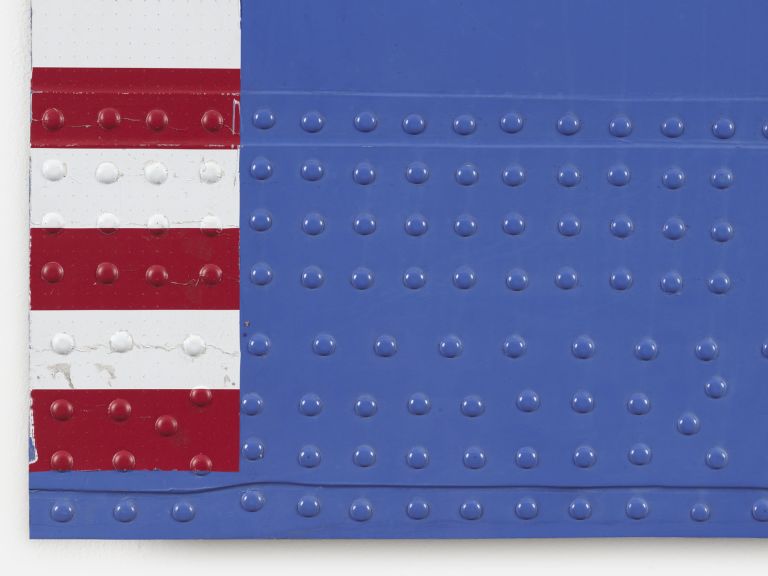 Abstract art piece featuring a blue rectangular field with red and white stripes on the left side. The surface has visible rivets or dots, suggesting industrial materials