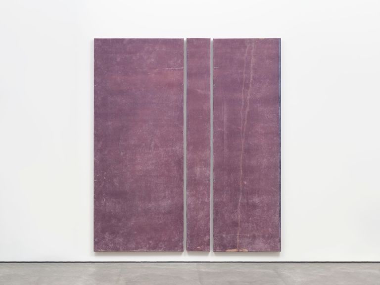 Three large purple abstract paintings mounted on white gallery wall, displaying mottled, cloud-like purple tones and textures.