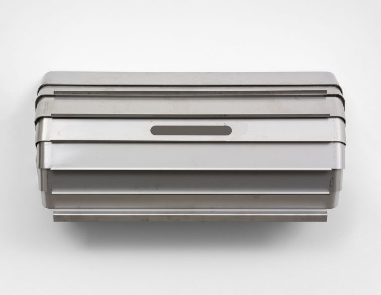 Geometric metal wall sculpture with layered angular forms in silver/gray finish, creating dimensional shadow patterns.