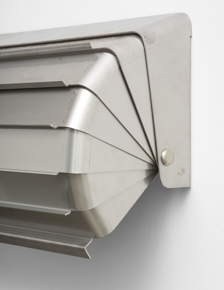 Geometric metal wall sculpture with layered angular forms in silver/gray finish, creating dimensional shadow patterns.