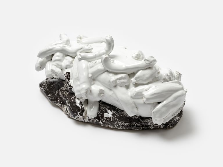 A black and white sculptural ceramic object with protruding elements resembling bones or limbs, partially resting on a black base, photographed against a white background.
