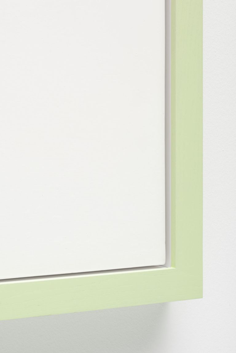 Minimalist white square artwork with green colored borders mounted on white wall. It features a small black hole near the left edge.