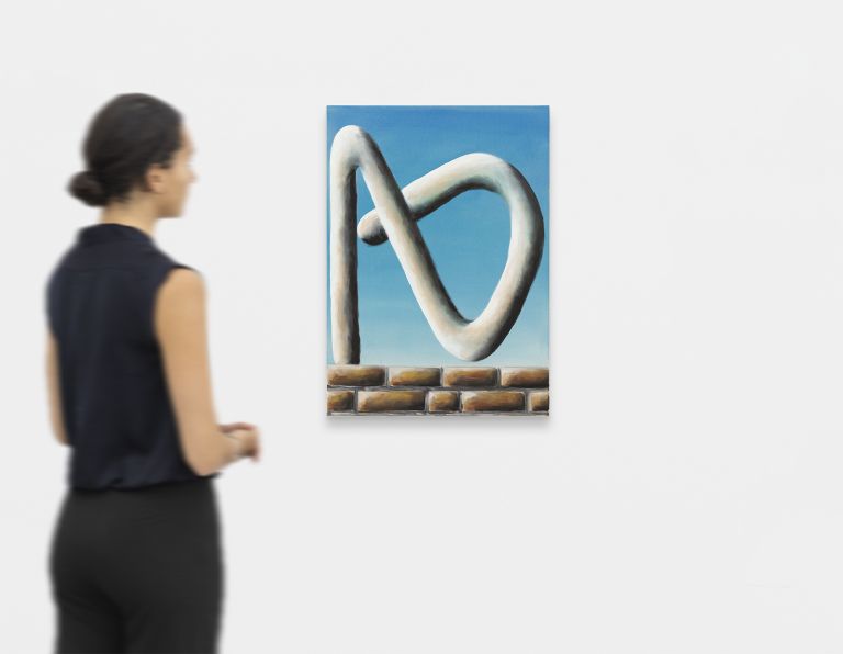 Painting showing white curved sculptural form resembling interconnected loops against blue sky, sitting on brick wall base