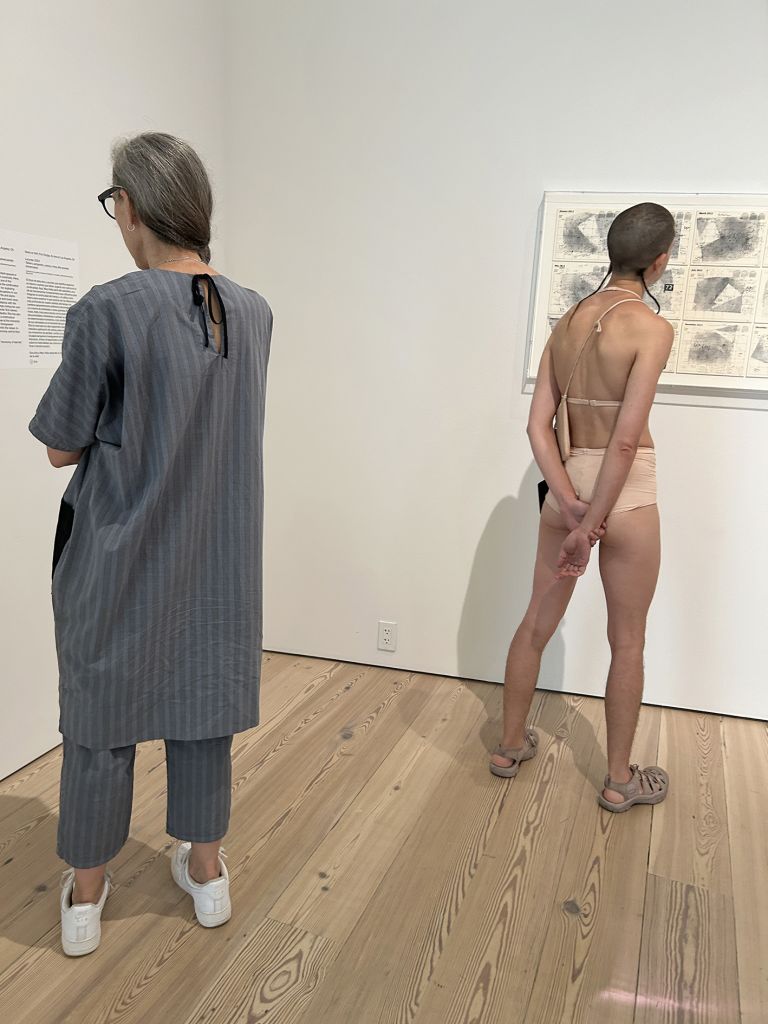 Black-framed display showing text and multiple photographs documenting performance art in various indoor gallery and museum settings.