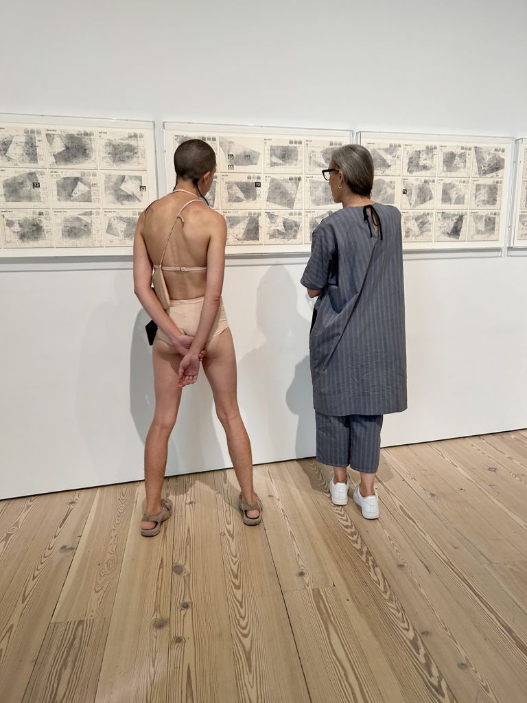 Black-framed display showing text and multiple photographs documenting performance art in various indoor gallery and museum settings.