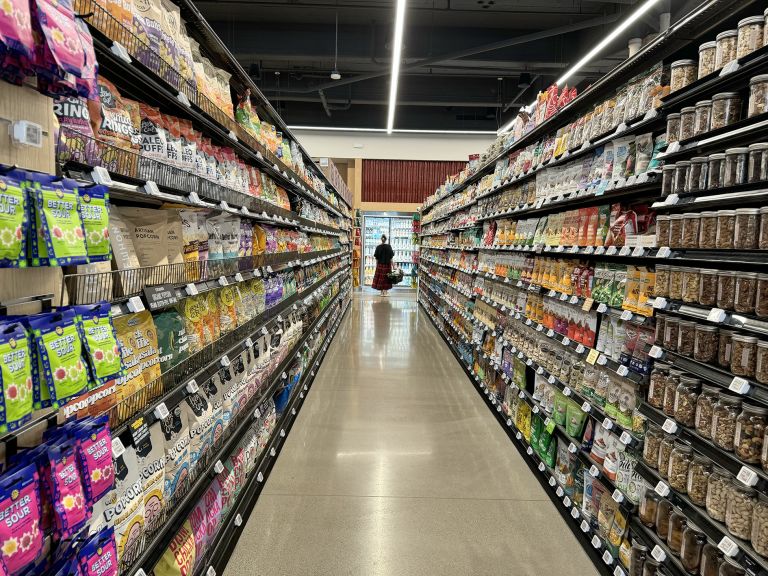 Large horizontal frame containing text panel and photographs showing grocery store performances with produce sections and shopping aisles.