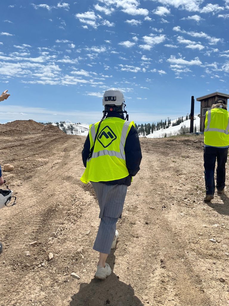 Frame displaying text and photographs of construction or work site performance with people in safety vests in mountainous terrain.