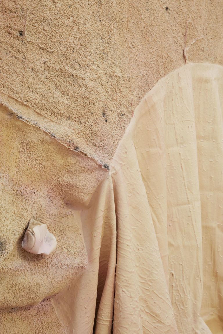 Close-up of arched wall niche with draped pink/beige fabric sculpture and small objects mounted above.