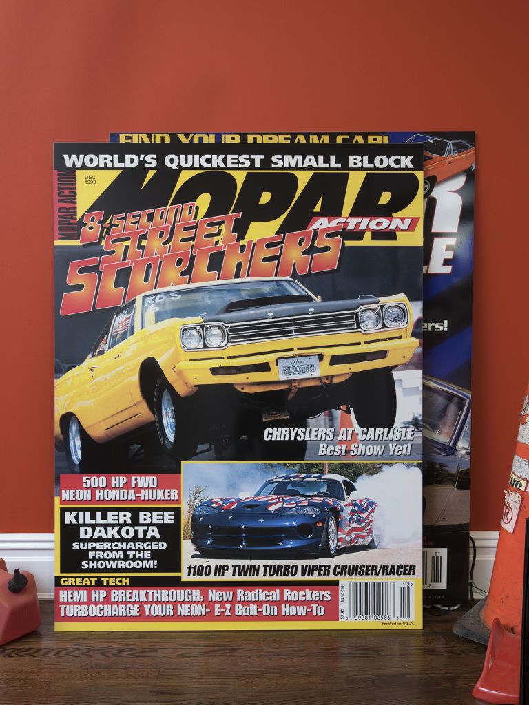 Red wall with "SHE-DEVILS ON WHEELS" text above cluttered desk with tire, racing gear and memorabilia.