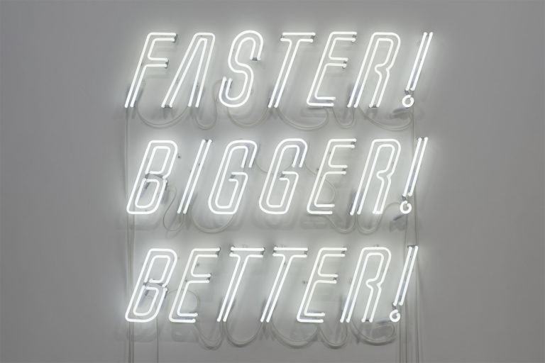 White neon sign reading "FASTER! BIGGER! BETTER!" in stacked italic letters against gray wall.